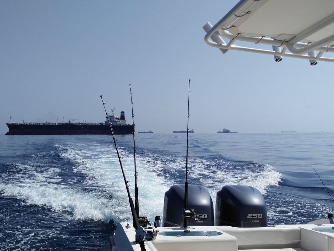 Rods set in the holders on a fishing boat off Fujairah, tanker anchorage on the horizon