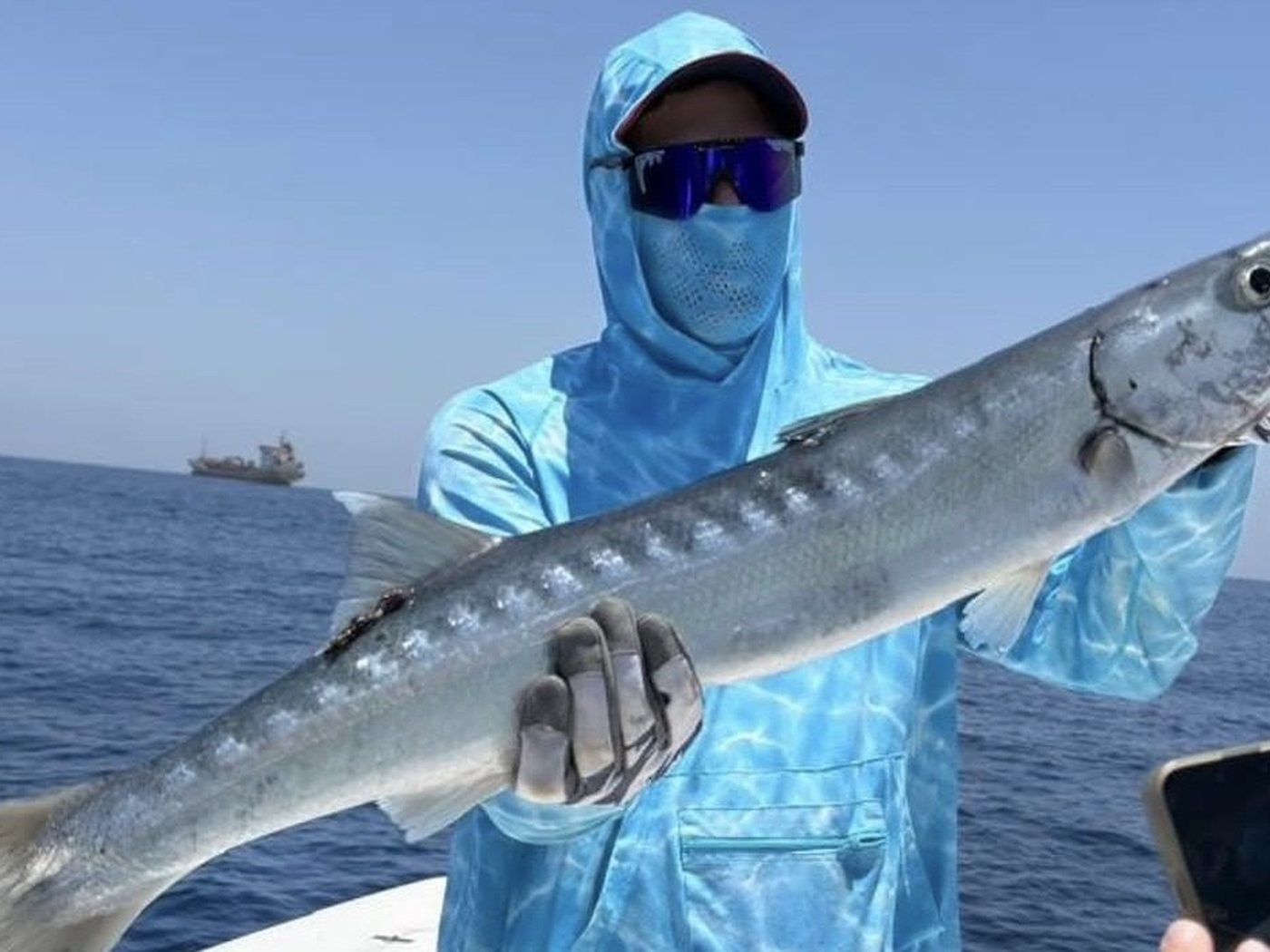 A barracuda held up on a fishing boat off Fujairah, tanker on the horizon