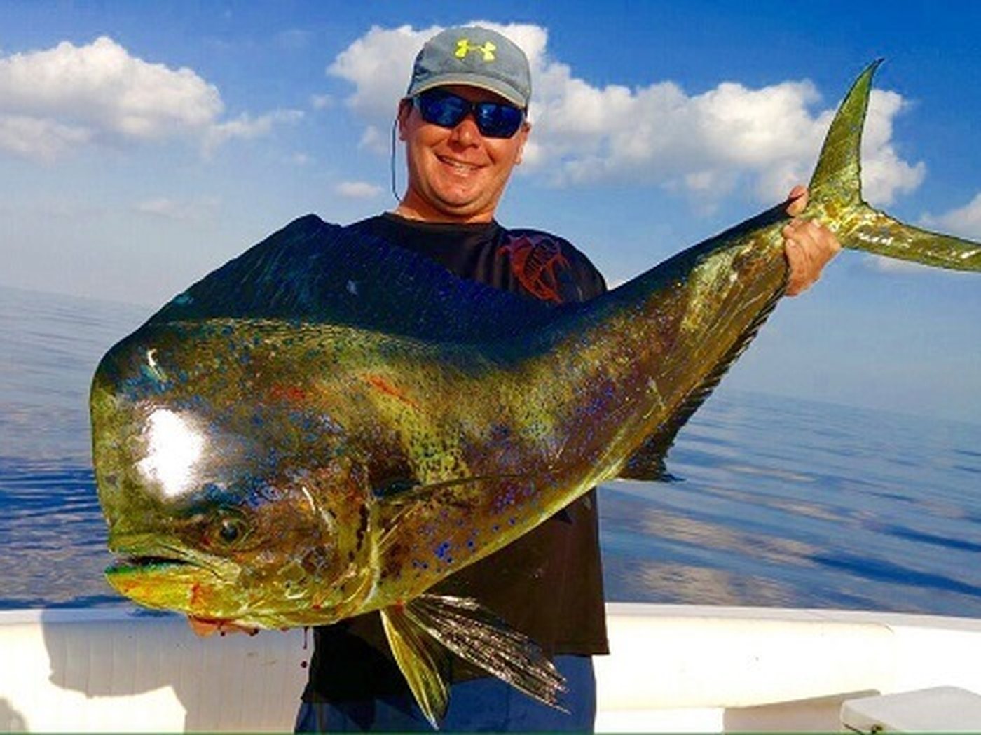 A guest holding a dorado on the deck, open blue water behind