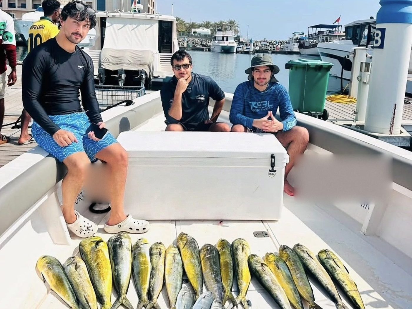 Three guests on a fishing boat at Fujairah marina with the morning's dorado laid out on deck