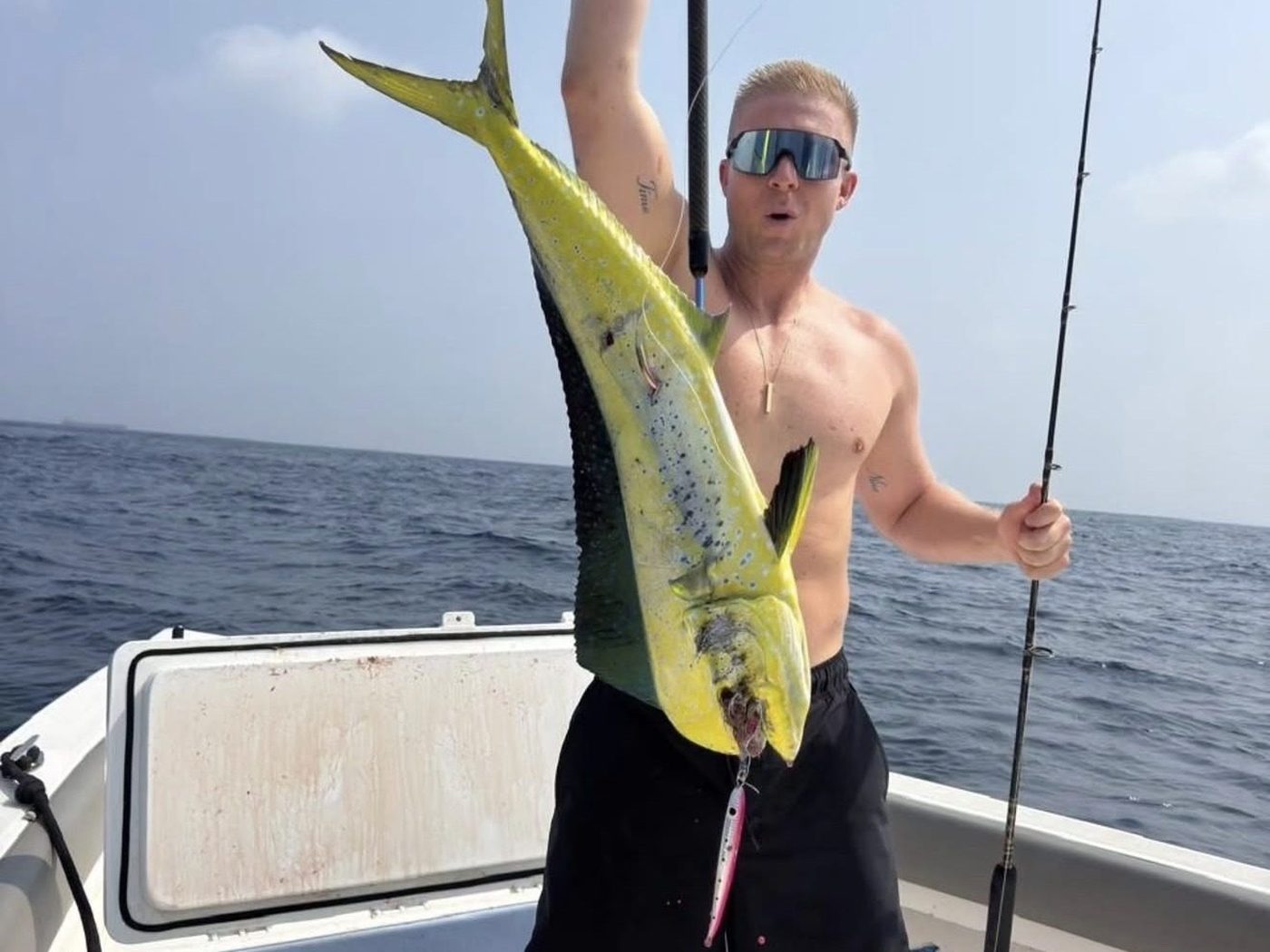 A guest holding a dorado by the tail on the deck, rod still in hand