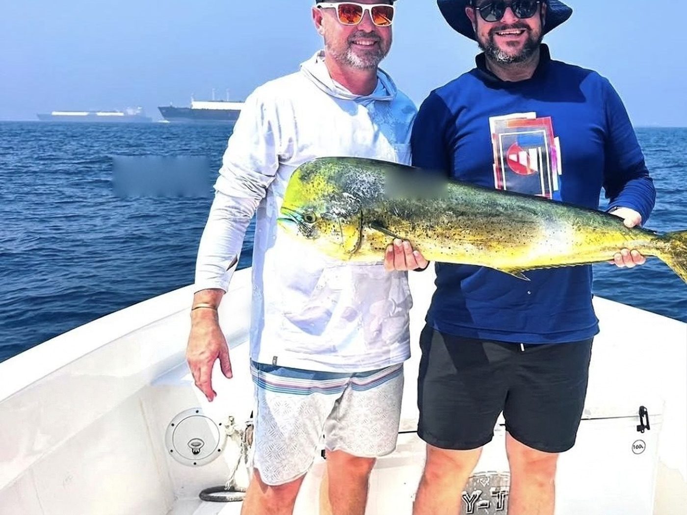 Two guests holding a dorado on a fishing boat off Fujairah, tanker anchorage behind