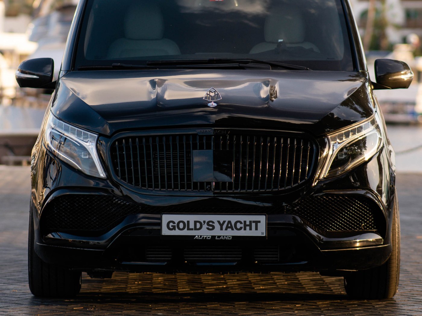 A black Mercedes V-class transfer van for Gold's Yacht guests, Dubai marina behind