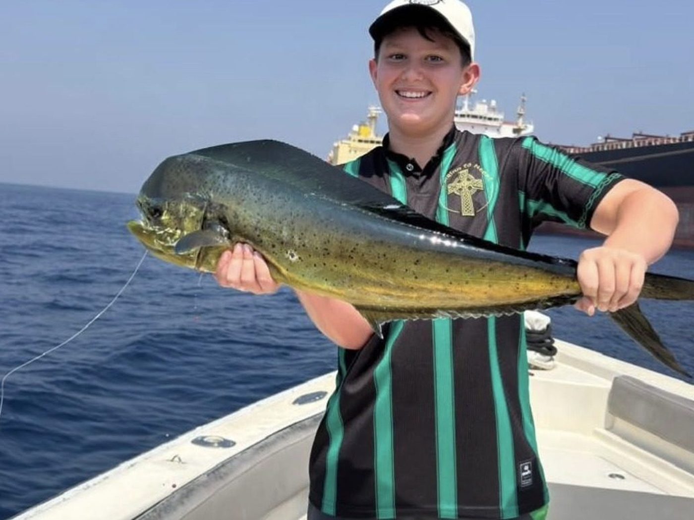 A young angler holding a dorado on the deck of a fishing boat in Fujairah