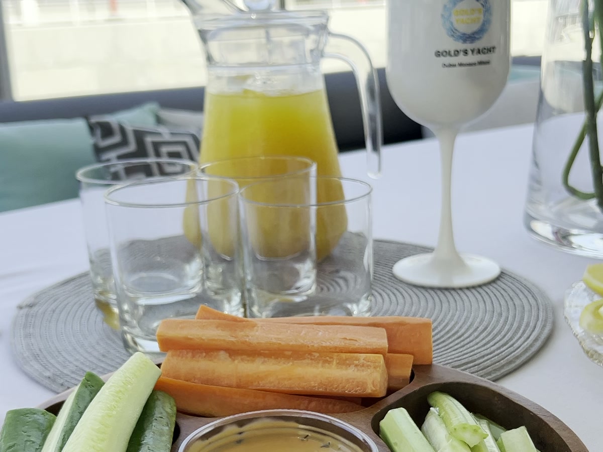 Crudites platter with dip beside a juice jug and branded glassware on deck
